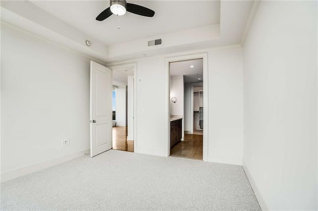 unfurnished bedroom featuring a raised ceiling, connected bathroom, ceiling fan, and light colored carpet