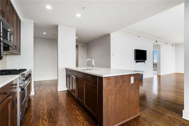 kitchen featuring appliances with stainless steel finishes, dark hardwood / wood-style flooring, dark brown cabinetry, sink, and a center island with sink