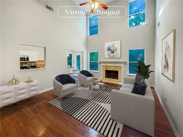 living room with ceiling fan, a towering ceiling, dark wood-type flooring, and a fireplace