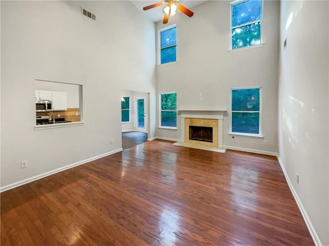 unfurnished living room featuring a high ceiling, wood-type flooring, a premium fireplace, and ceiling fan