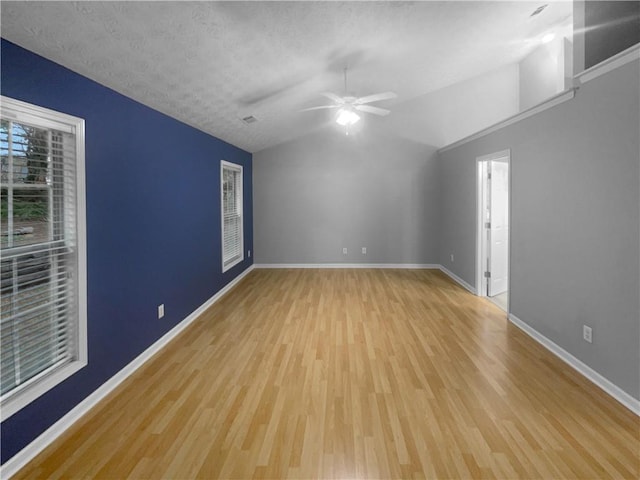 unfurnished room with lofted ceiling, a textured ceiling, wood finished floors, and baseboards