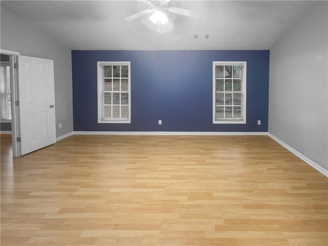 spare room featuring light wood finished floors, visible vents, baseboards, ceiling fan, and vaulted ceiling