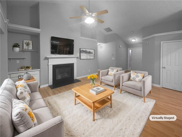 living room featuring a glass covered fireplace, visible vents, light wood-style flooring, and baseboards