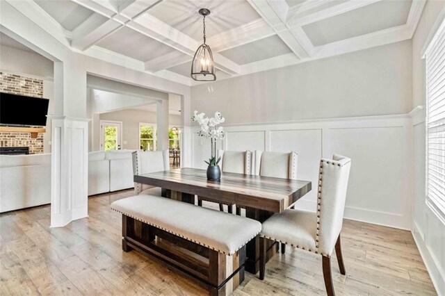 dining space featuring beamed ceiling, light hardwood / wood-style floors, coffered ceiling, and a fireplace