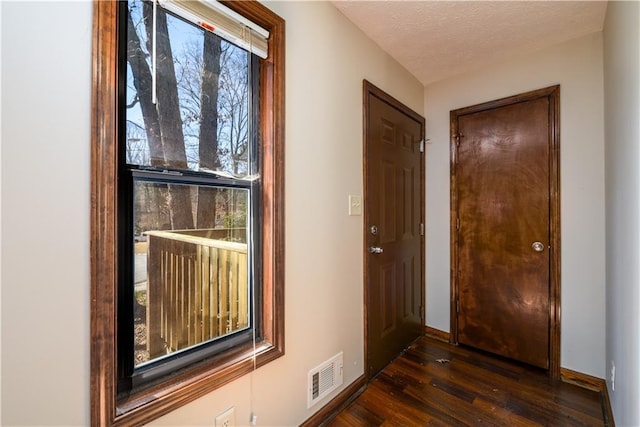 corridor featuring dark wood-type flooring, baseboards, visible vents, and a textured ceiling