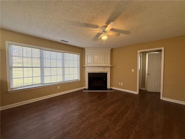 unfurnished living room with ceiling fan, dark wood-type flooring, a fireplace, visible vents, and baseboards