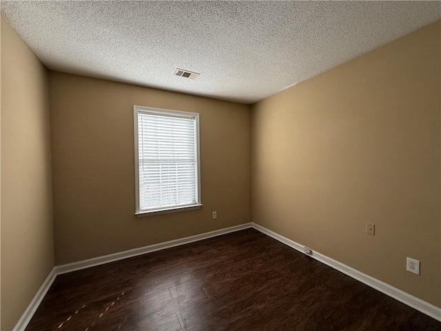 unfurnished room with a textured ceiling, dark wood-type flooring, visible vents, and baseboards