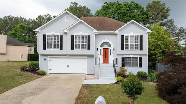 split foyer home featuring a garage, driveway, a front yard, and stucco siding