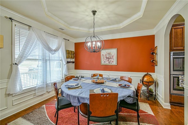 dining room with ornamental molding, a tray ceiling, an inviting chandelier, and dark wood-type flooring