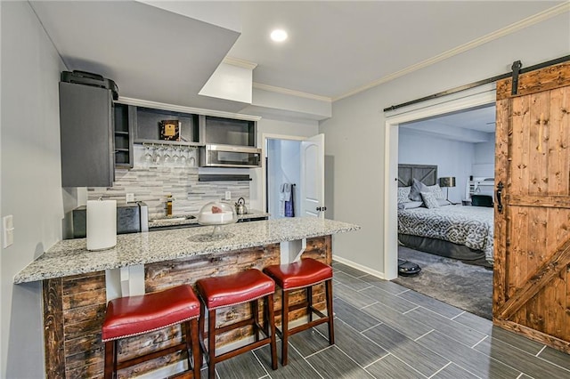 kitchen with a kitchen bar, kitchen peninsula, light stone countertops, backsplash, and a barn door