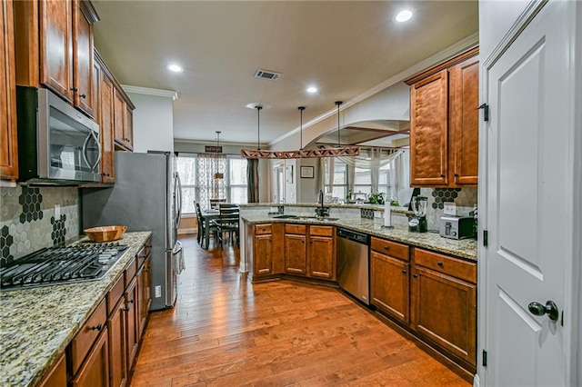 kitchen with pendant lighting, crown molding, kitchen peninsula, wood-type flooring, and stainless steel appliances