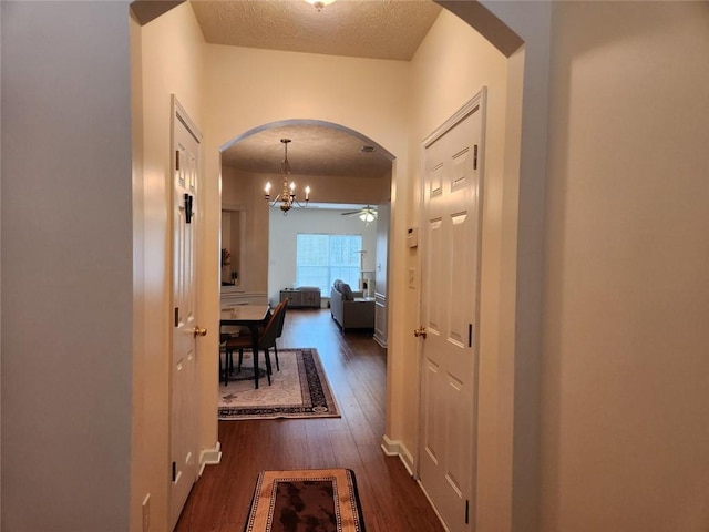 hallway featuring an inviting chandelier, dark hardwood / wood-style flooring, and a textured ceiling