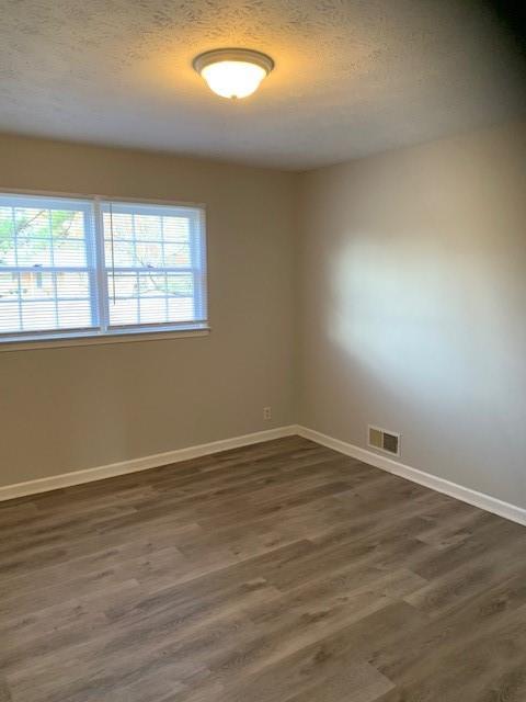 spare room featuring a textured ceiling and dark hardwood / wood-style floors