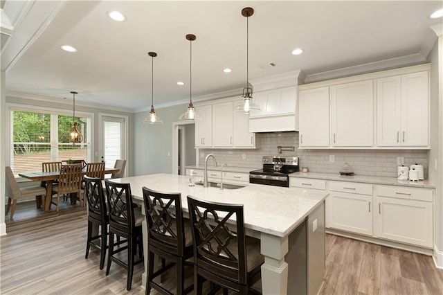 kitchen featuring stainless steel electric range oven, a sink, light wood-type flooring, crown molding, and tasteful backsplash