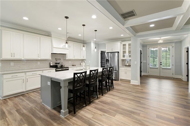 kitchen with appliances with stainless steel finishes, crown molding, a kitchen bar, backsplash, and light wood-type flooring