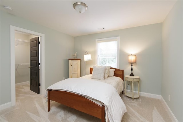 bedroom with light carpet, a walk in closet, baseboards, and a closet