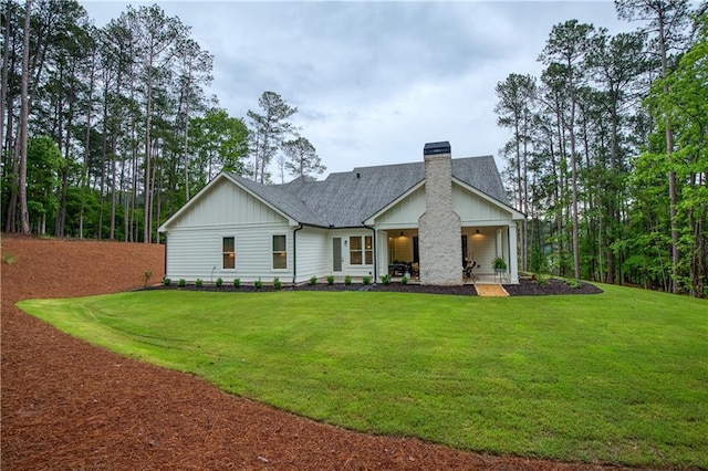 rear view of property with board and batten siding, a chimney, a lawn, and a shingled roof