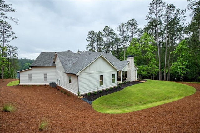 view of side of home with board and batten siding, roof with shingles, a yard, and a chimney