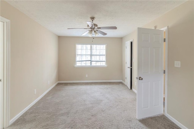 empty room with ceiling fan, light carpet, baseboards, and a textured ceiling