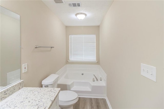 bathroom with visible vents, toilet, a garden tub, a textured ceiling, and vanity