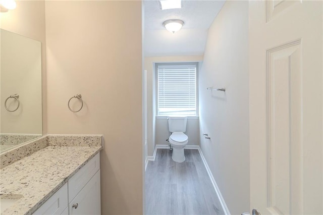 bathroom with vanity, toilet, wood finished floors, and baseboards