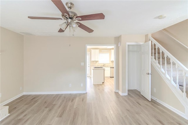 empty room with stairway, light wood-style flooring, a ceiling fan, and baseboards