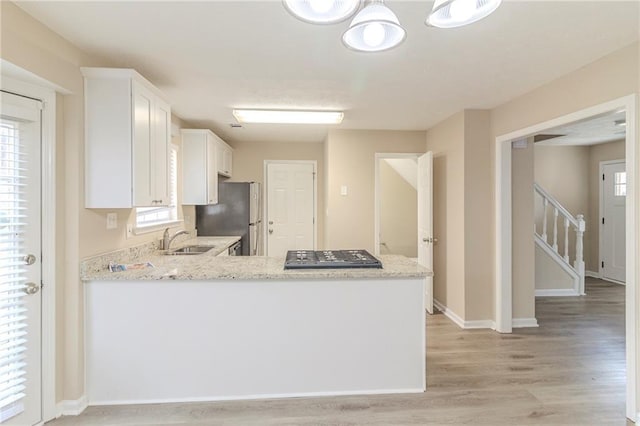 kitchen featuring light wood-type flooring, a sink, white cabinetry, freestanding refrigerator, and light stone countertops