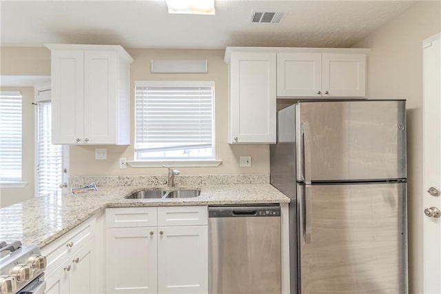 kitchen featuring visible vents, a sink, white cabinetry, stainless steel appliances, and light stone countertops