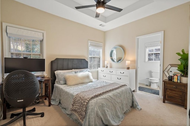 carpeted bedroom featuring ceiling fan, ensuite bath, and a raised ceiling