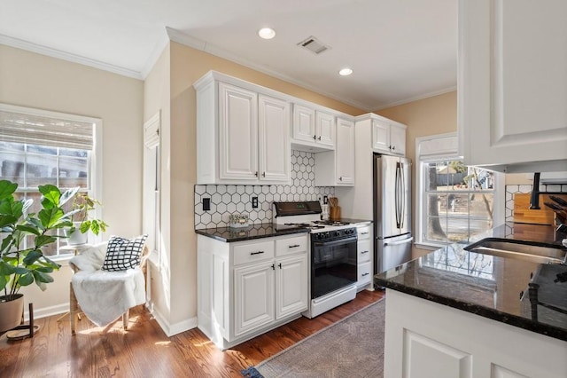 kitchen with stainless steel refrigerator, white cabinetry, dark stone counters, and gas range oven