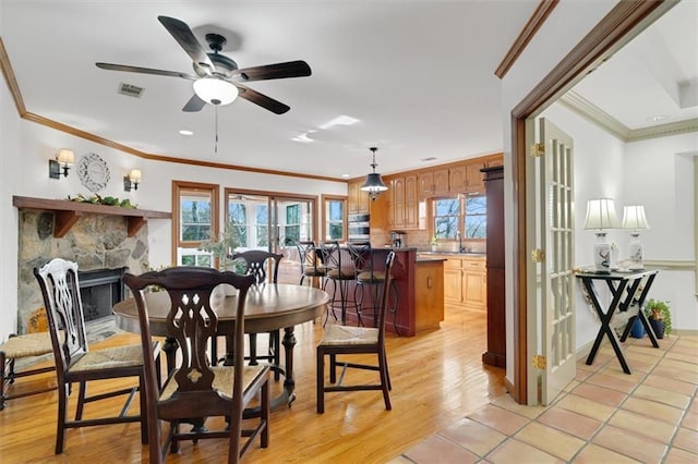 dining area with crown molding, a stone fireplace, ceiling fan, and light wood-type flooring