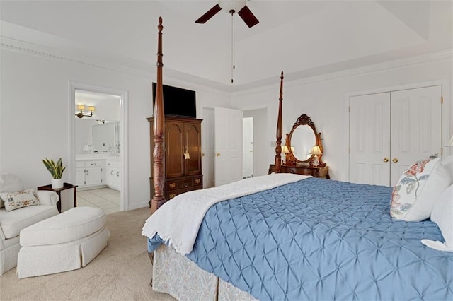 carpeted bedroom featuring ensuite bath, ceiling fan, a tray ceiling, ornamental molding, and a closet