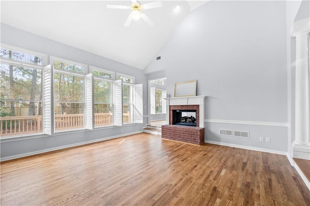 unfurnished living room with high vaulted ceiling, wood-type flooring, a fireplace, and decorative columns