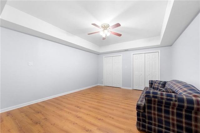 sitting room with light hardwood / wood-style floors, a raised ceiling, and ceiling fan