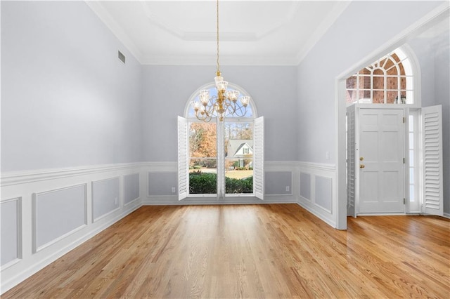 entryway featuring an inviting chandelier, light hardwood / wood-style flooring, ornamental molding, and a raised ceiling