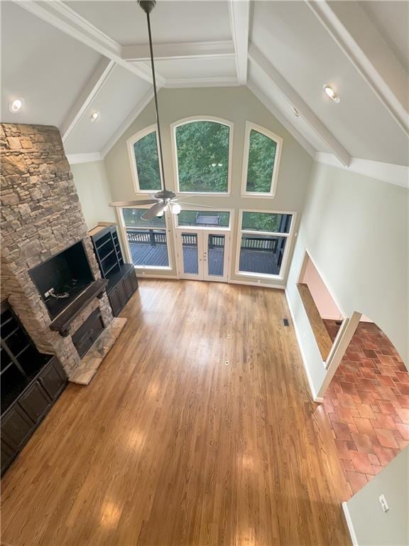 unfurnished living room featuring beam ceiling, ceiling fan, hardwood / wood-style floors, and a stone fireplace