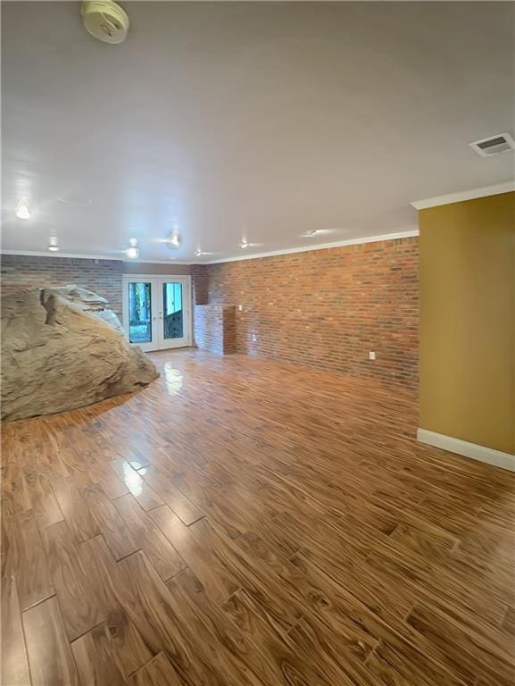 unfurnished living room with wood-type flooring, ornamental molding, and brick wall