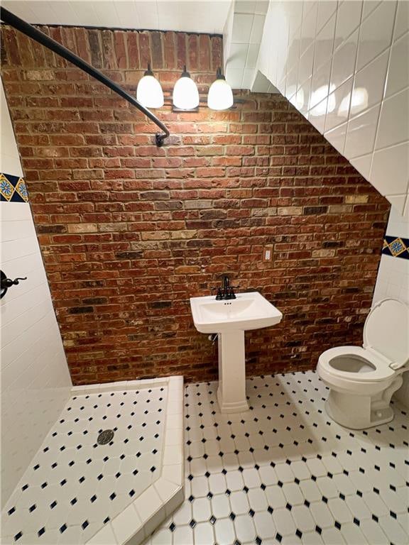 bathroom featuring walk in shower, brick wall, and toilet