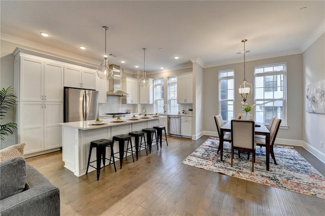 kitchen featuring a center island, wall chimney range hood, pendant lighting, stainless steel appliances, and white cabinets