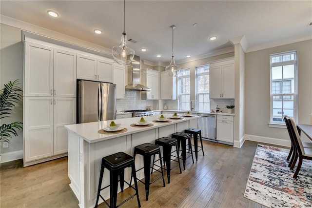 kitchen with wall chimney exhaust hood, white cabinetry, hanging light fixtures, appliances with stainless steel finishes, and a kitchen island