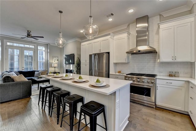 kitchen with white cabinets, a kitchen island, wall chimney exhaust hood, and appliances with stainless steel finishes