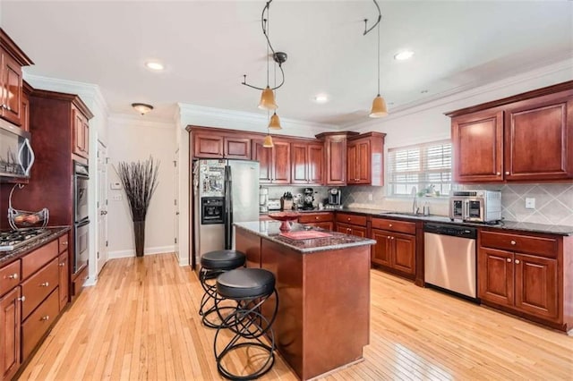 kitchen with appliances with stainless steel finishes, decorative light fixtures, light hardwood / wood-style floors, and a kitchen island