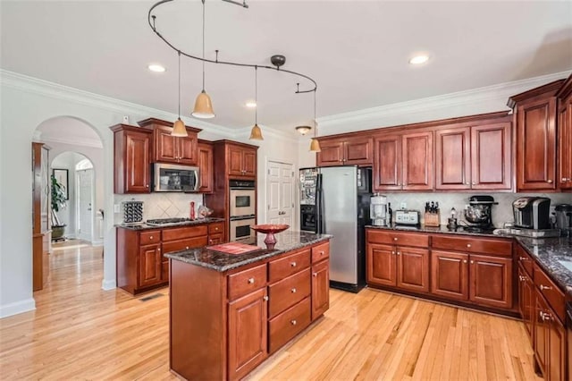 kitchen with appliances with stainless steel finishes, light wood-type flooring, a kitchen island, hanging light fixtures, and decorative backsplash