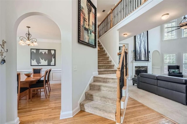 stairs featuring a towering ceiling, ornamental molding, wood-type flooring, and ceiling fan