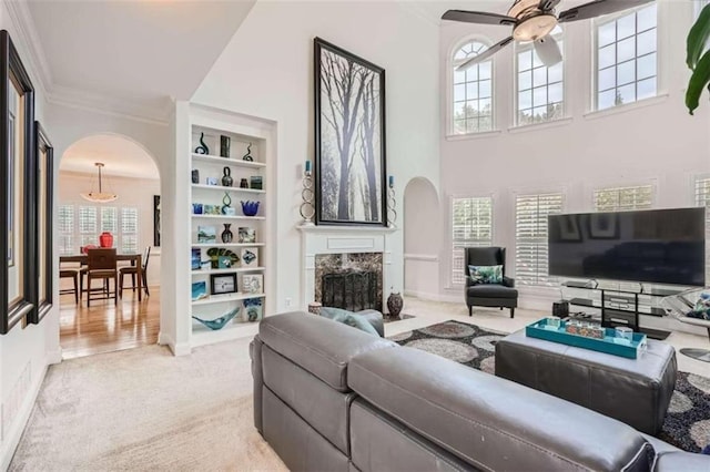 living room with a premium fireplace, ornamental molding, built in shelves, a towering ceiling, and light colored carpet