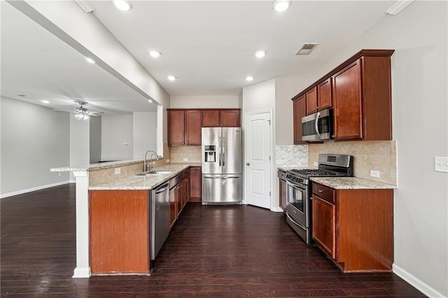 kitchen with a sink, light stone counters, dark wood finished floors, appliances with stainless steel finishes, and a peninsula