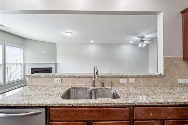 kitchen featuring light stone countertops, a fireplace, a sink, stainless steel dishwasher, and tasteful backsplash