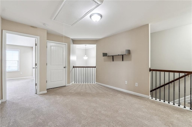 carpeted spare room featuring attic access and baseboards