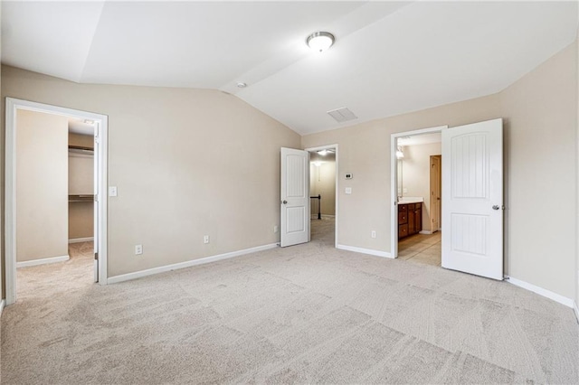 unfurnished bedroom featuring a walk in closet, baseboards, lofted ceiling, light carpet, and ensuite bath