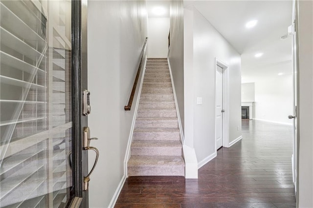 stairs with a glass covered fireplace, baseboards, hardwood / wood-style floors, and recessed lighting